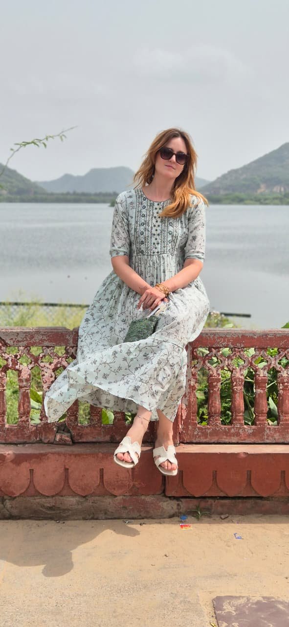 A woman in a floral dress sitting on a carved stone railing with Jal Mahal across the water in Jaipur