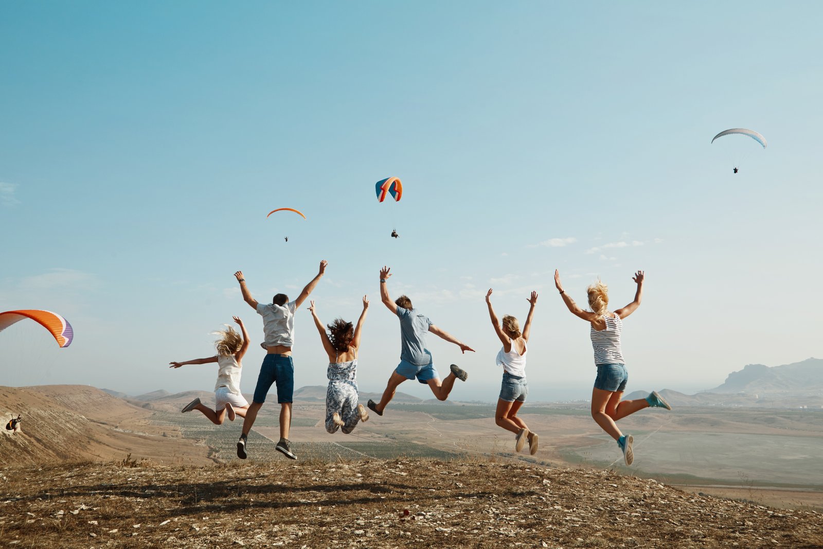 Travellers celebrating on a hilltop with paragliders — business beyond boardrooms